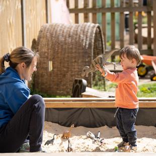 A person and a child playing with dinosaur toys in a sandbox.