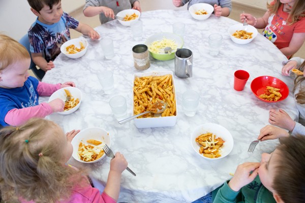 A group of children sitting around a table, eating pasta from bowls