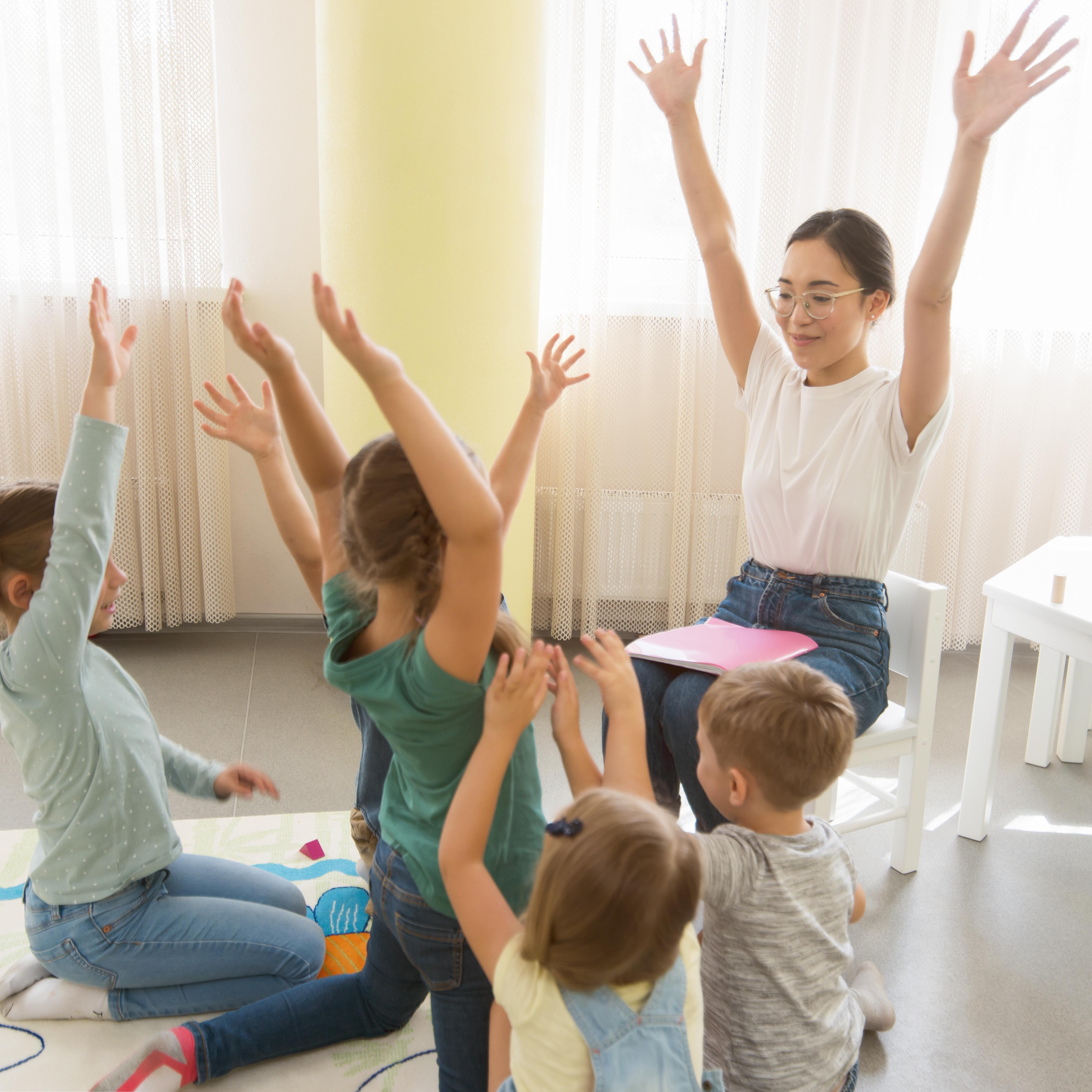 A group of young children and a teacher raising their arms in the air