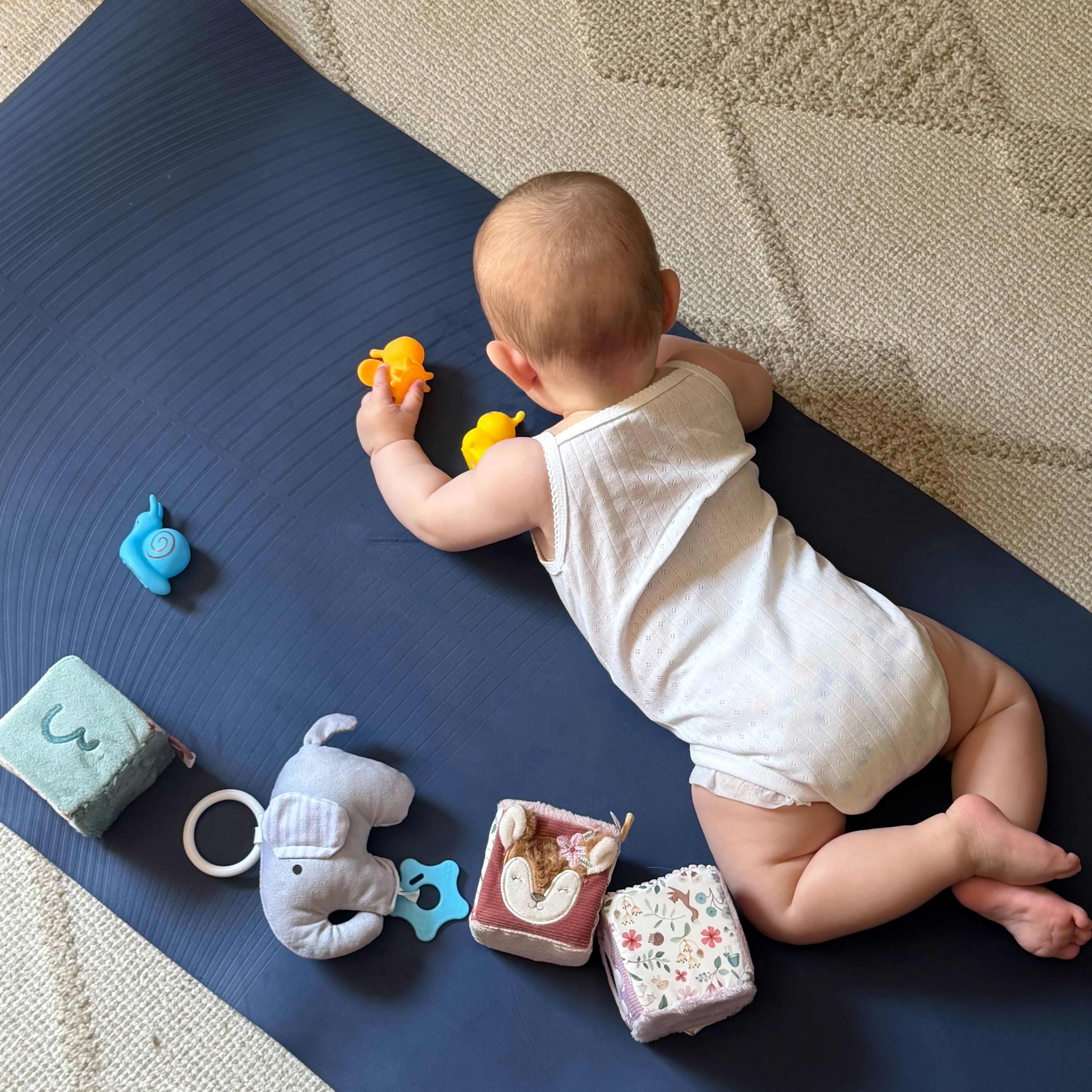 Baby playing with colourful toys on a blue mat.