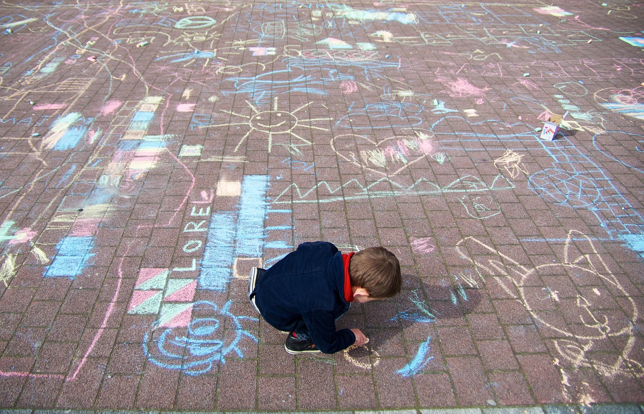 A child creating colourful chalk drawings on a paved surface filled with playful designs