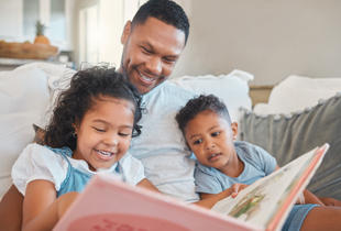 A parent reading to their young children on the sofa at home