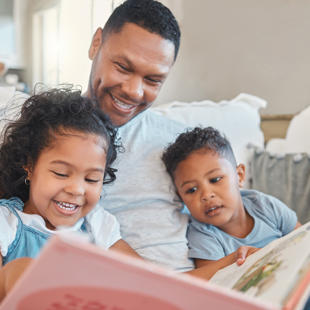A parent reading to their young children on the sofa at home