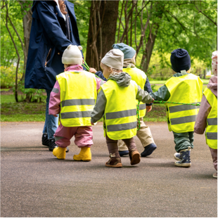 teacher leading a group of children in yellow safety vests on a walk, children holding a rope for safety