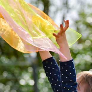 A child reaching up for a coloured scarf in the sunshine