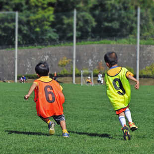 two young children in bright orange and yellow bibs running on a sports field