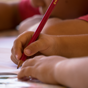 child's hands drawing on paper with a pencil