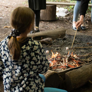 A group of people around a fire pit toasting marshmallows