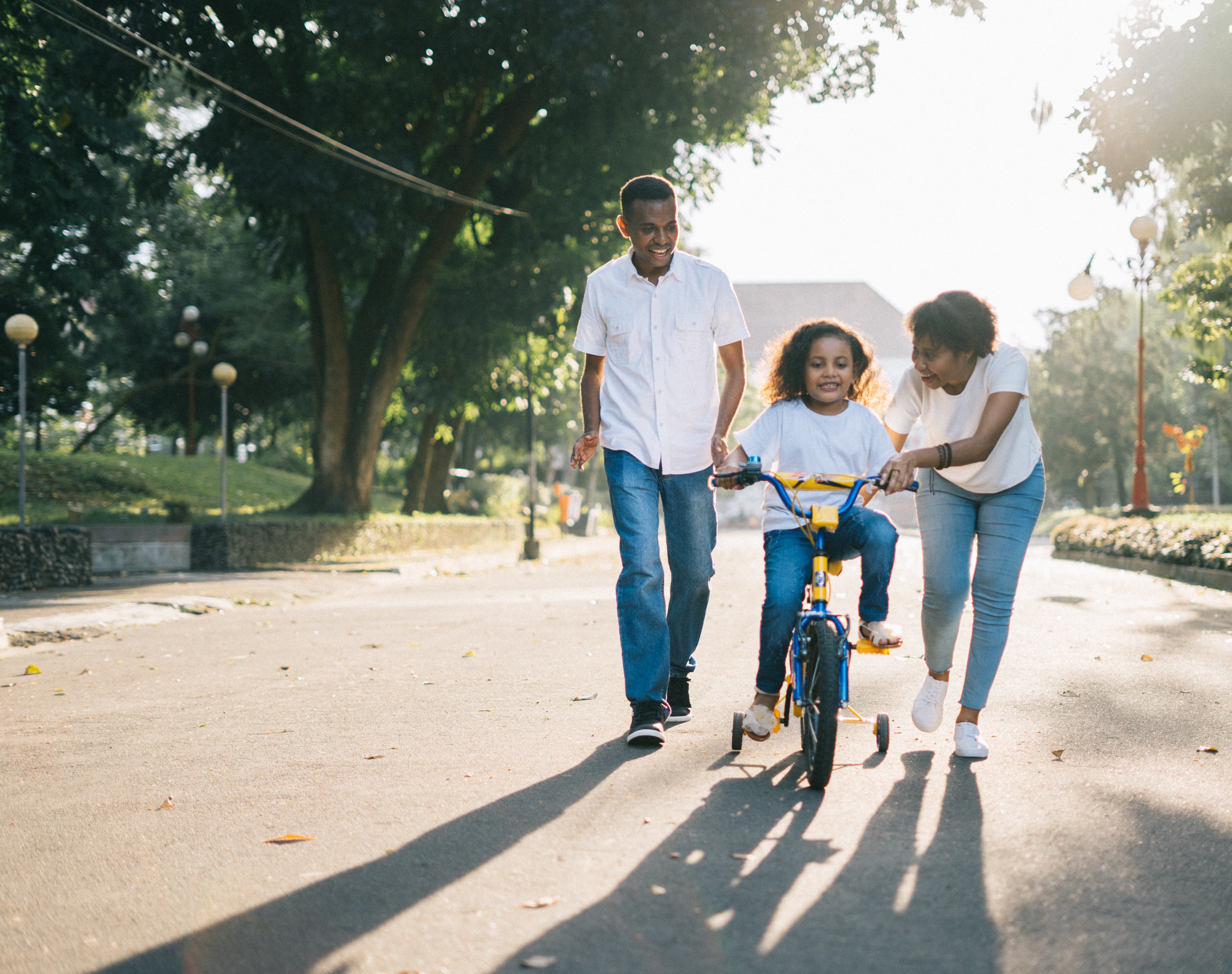 A couple of adults assisting a young child riding a bicycle.