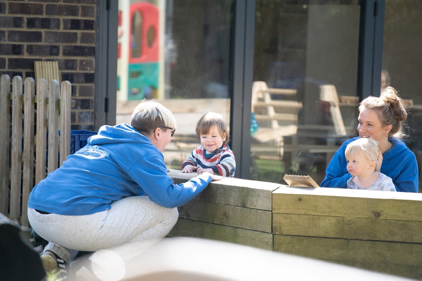 Two adults and children sitting along a wooden wall
