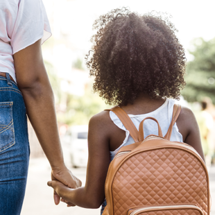young child with backpack holding a person's hand