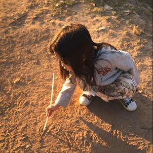 A young child drawing in sand with a stick