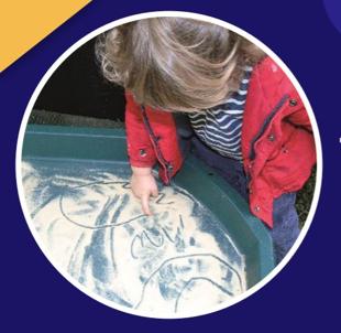 Young child using their finger to draw in a sandbox