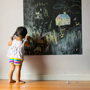 baby pupil draws with chalk on a blackboard